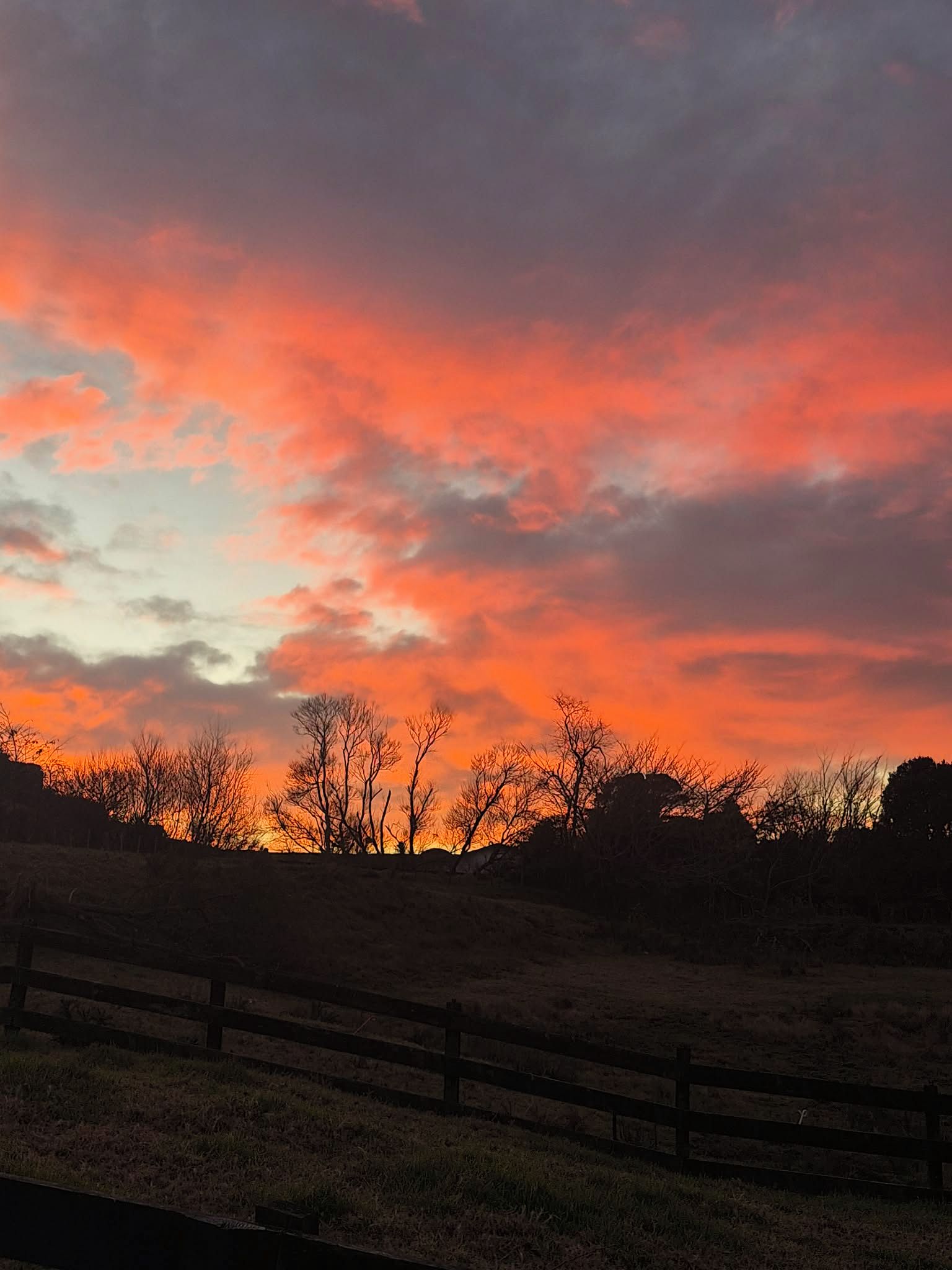 A sunset with a wooden fence in the foreground.