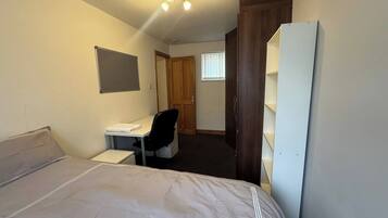 A hotel room with a bed, a desk, a chair, a wardrobe, and a window.