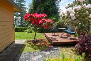 A patio area with a wooden deck, outdoor furniture, and a small tree with red flowers. - Zen Suite at Buckhorn Cove near Mendocino w/ Ocean View, Full Kitchen, sleeps 4 (Mendocino County)