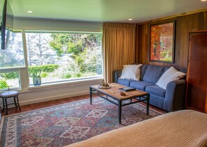A room with a sofa, a coffee table, a window with curtains, a rug, and a painting on the wall. - Zen Suite at Buckhorn Cove near Mendocino w/ Ocean View, Full Kitchen, sleeps 4 (Mendocino County)
