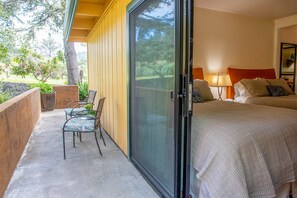 A bedroom with a bed, a chair, and a sliding glass door leading to an outdoor area with a chair and plants. - Forest Den at Buckhorn Cove near Mendocino - cozy gas fireplace & sleeps 4 (Mendocino County)
