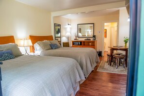 A hotel room with two beds, a desk with a chair, a mirror, and a small table with a vase of flowers. - Forest Den at Buckhorn Cove near Mendocino - cozy gas fireplace & sleeps 4 (Mendocino County)