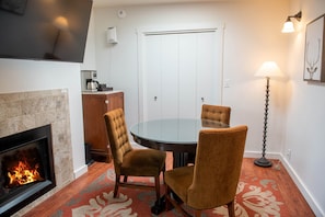 A cozy room with a fireplace, a round glass table, and two upholstered chairs.