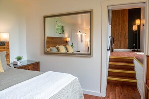 A hotel room with a large mirror, a bed with patterned bedding, a bedside table with a lamp, and a view of the hallway and stairs. - Bay View Suite at Buckhorn Cove Inn near Mendocino Sleeps 3, Ocean View, EV Chgr (Mendocino County)