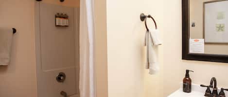 A bathroom with a shower, a sink, a mirror, and a towel rack.