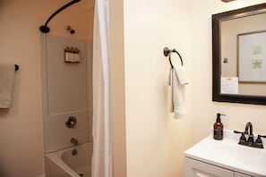 A bathroom with a shower, a sink, a mirror, and a towel rack.