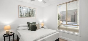 Ein Schlafzimmer mit einem Bett, zwei Nachttischen, einem Deckenventilator, einem Fenster mit Jalousien und einem gerahmten Bild an der Wand.