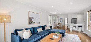 Ein modernes Wohnzimmer mit einer blauen Sofagarnitur, einem Holztisch und einem Essbereich mit weißem Tisch und Stühlen.