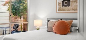 A bedroom with a bed, a bedside lamp, a window with a view of trees, and a framed picture on the wall. - Mia’s Place: Modern Pet-Friendly Geelong West Stay (Greater Geelong)