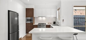 Una cucina moderna con mobili bianchi, un frigorifero in acciaio inossidabile, un forno a microonde, un forno e un lavello.