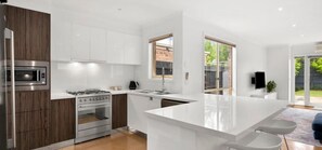 A modern kitchen with white cabinetry, a central island, and a built-in oven. - Mia’s Place: Modern Pet-Friendly Geelong West Stay (Greater Geelong)