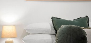 Un letto con cuscini bianchi e verdi, una lampada e una testiera.