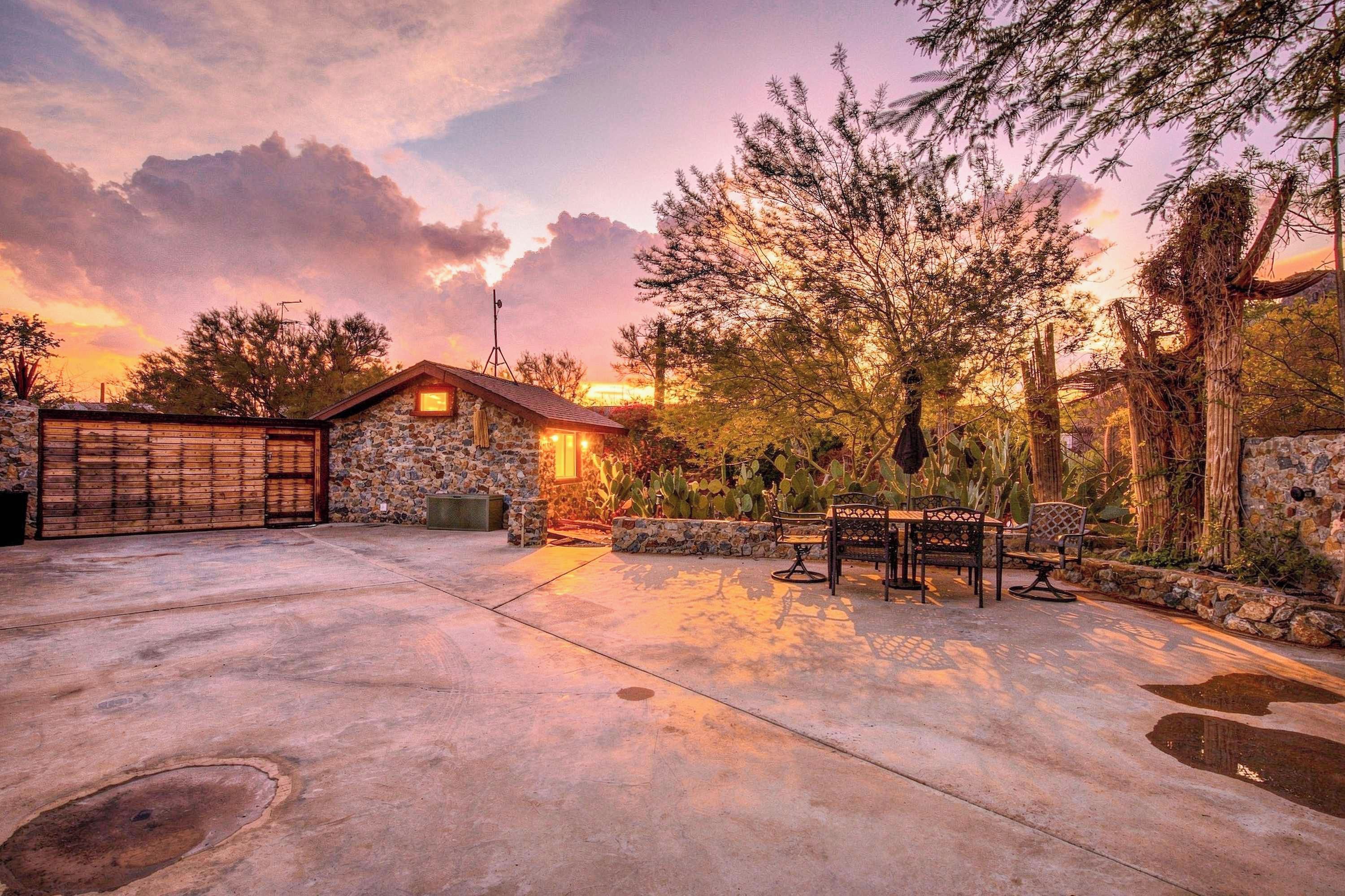 A stone building with a wooden door, surrounded by a paved area and cacti.