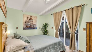Ein Schlafzimmer mit einem Bett, einem Wandbild, einer Topfpflanze und Blick durch eine Glastür.