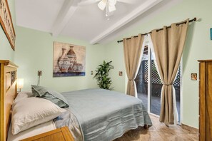 A bedroom with a bed, a wall-mounted painting, a potted plant, and a view through a glass door. - Desert Retreat | Hot Tub & Mountain Views (Tucson)