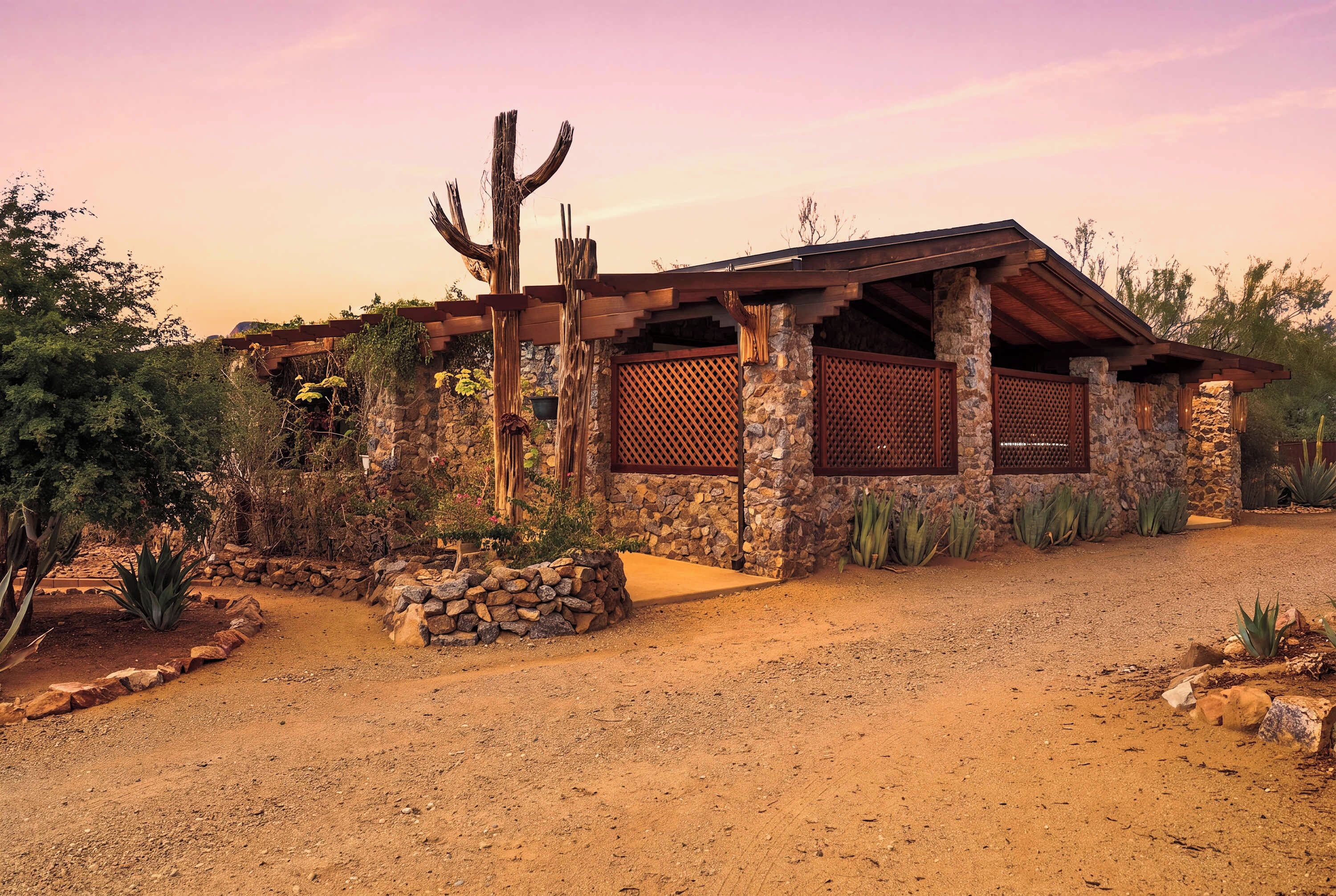 A desert-style house with a stone facade, wooden beams, and a cactus in the yard.