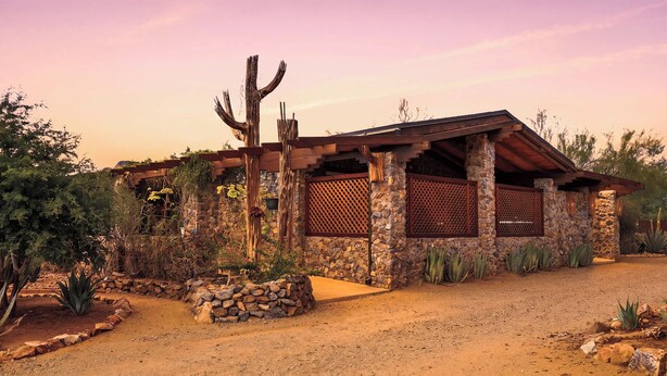 Ein Haus im Wüstendesign mit einer Stein-Fassade, Holzbalken und einem Kaktus im Garten.