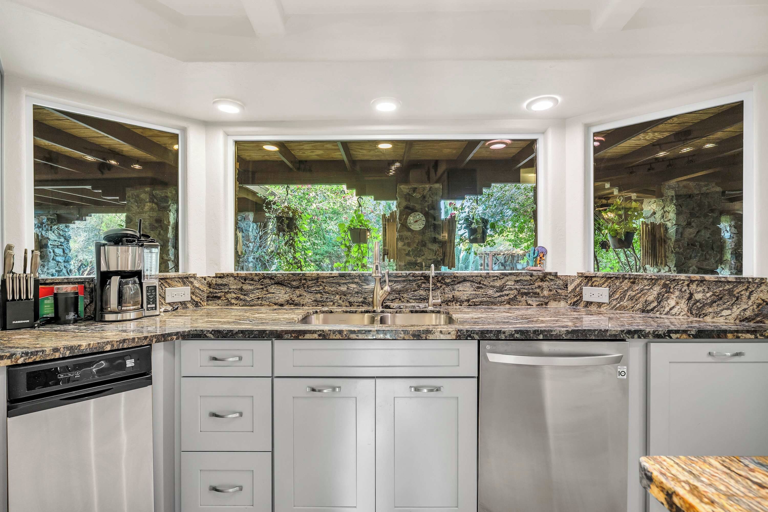 A kitchen with a granite countertop, stainless steel appliances, and a view of greenery through large windows.