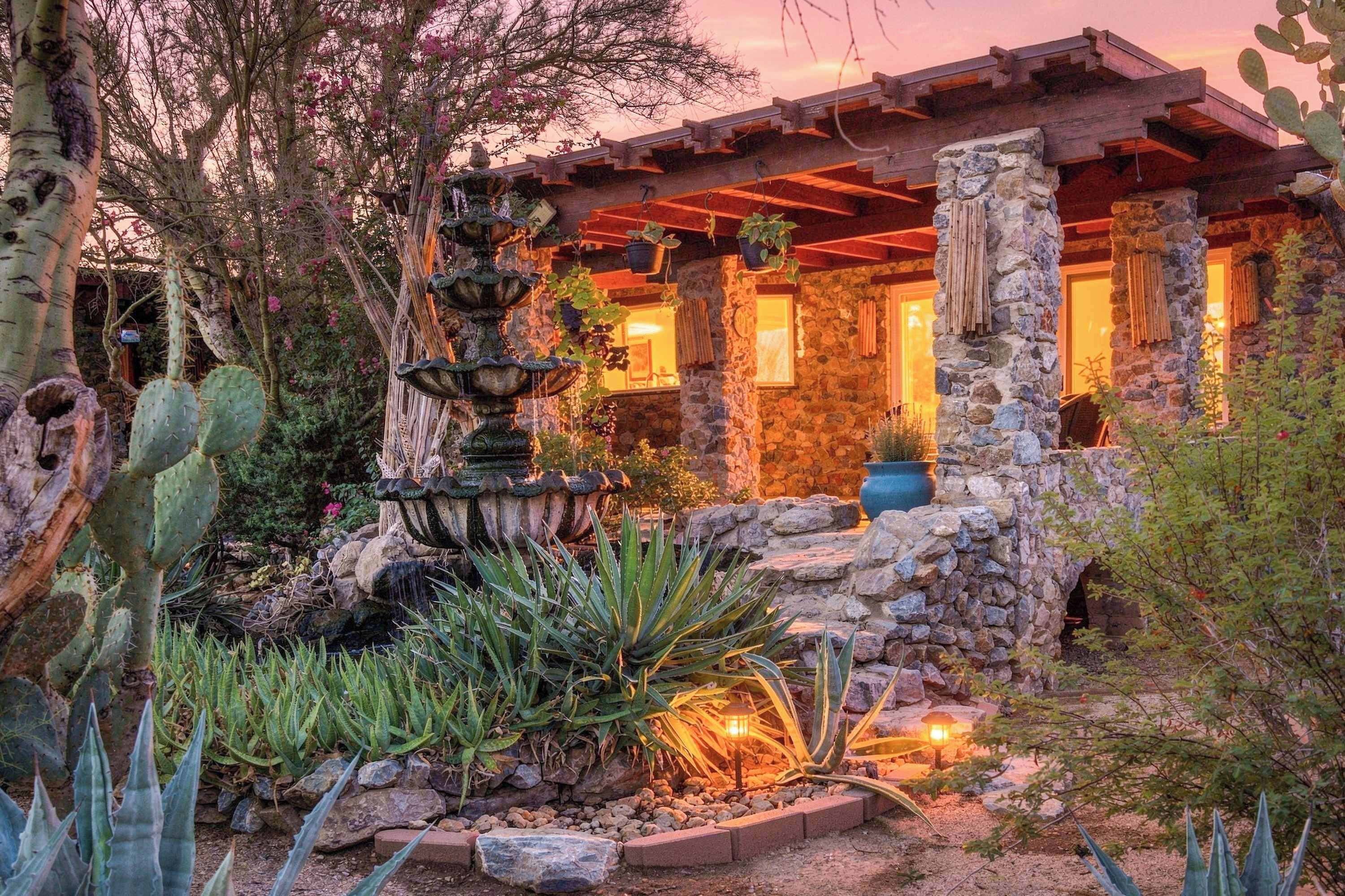 A stone building with a water feature in front, surrounded by desert plants.