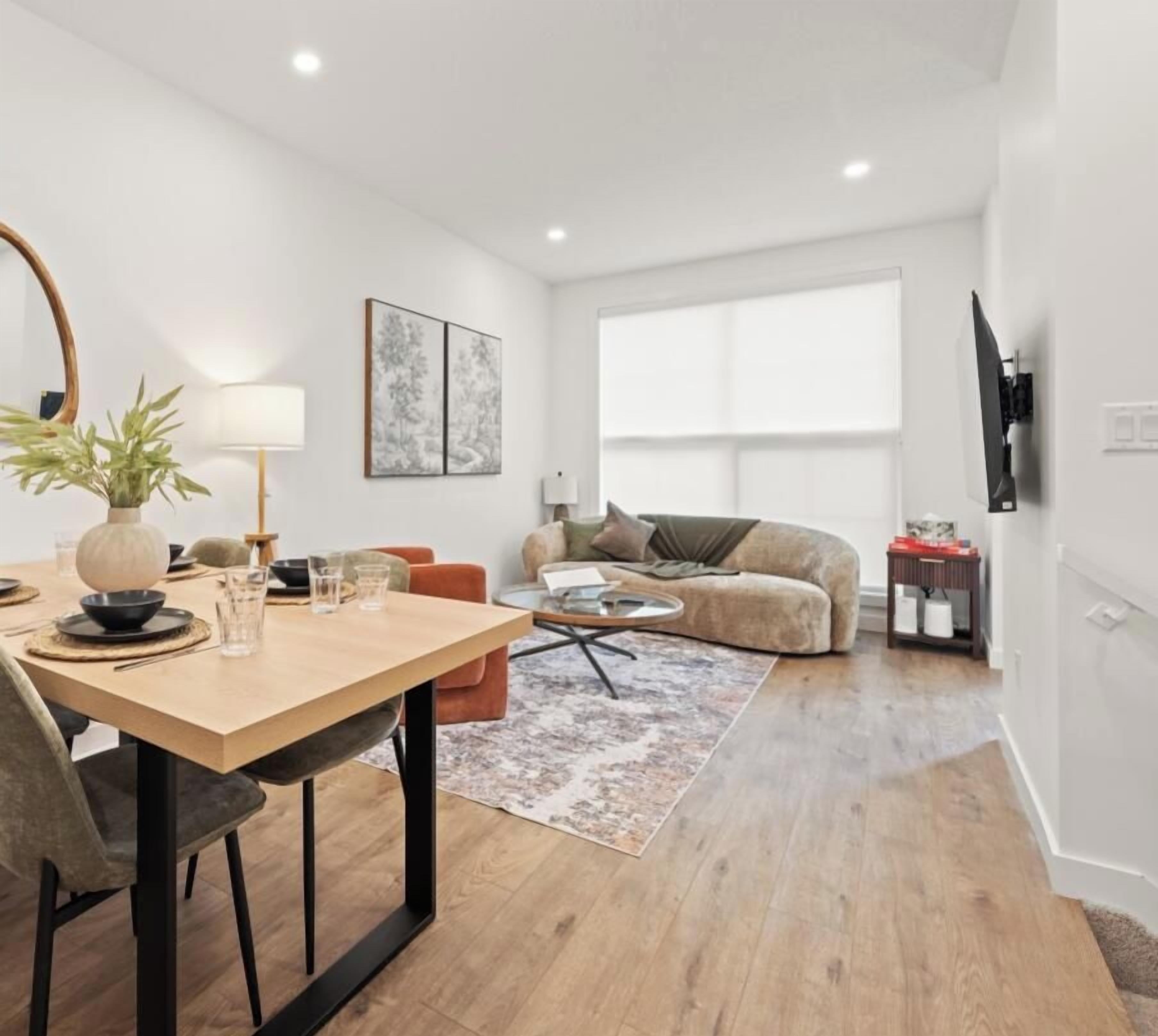 A modern living room with a dining area, a sofa, a TV, and a large window.