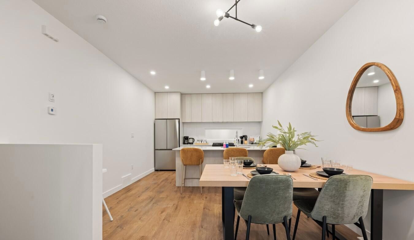 A modern kitchen with white cabinets, a central island, and a dining area with a wooden table and chairs.