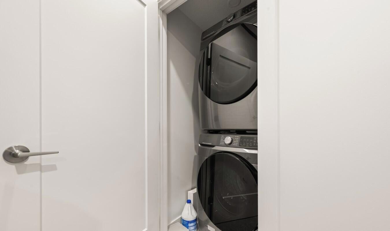 A closed door with a metallic handle, a washing machine, and a bottle of detergent on the floor.