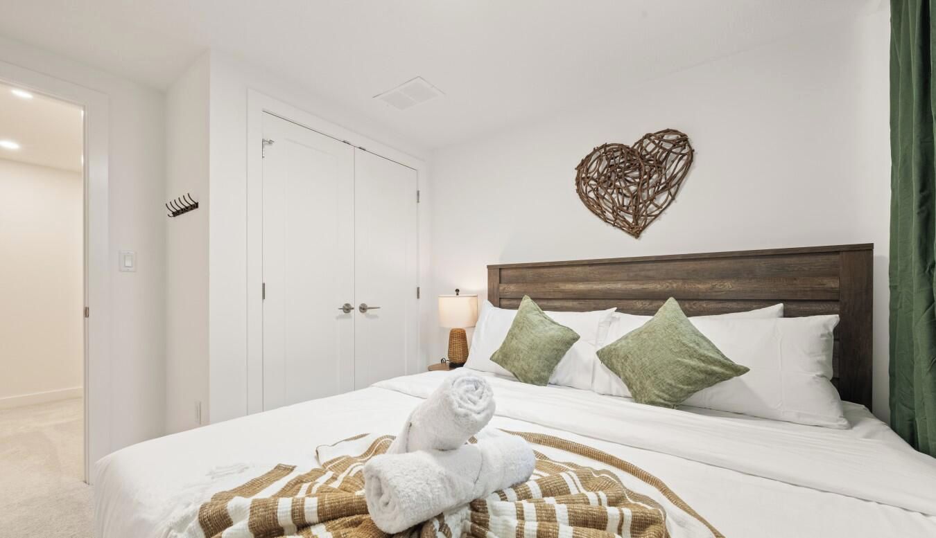 Ein Hotelzimmer mit Bett, weißen Wänden, einem Holzkopfteil und einer herzförmigen Dekoration an der Wand.