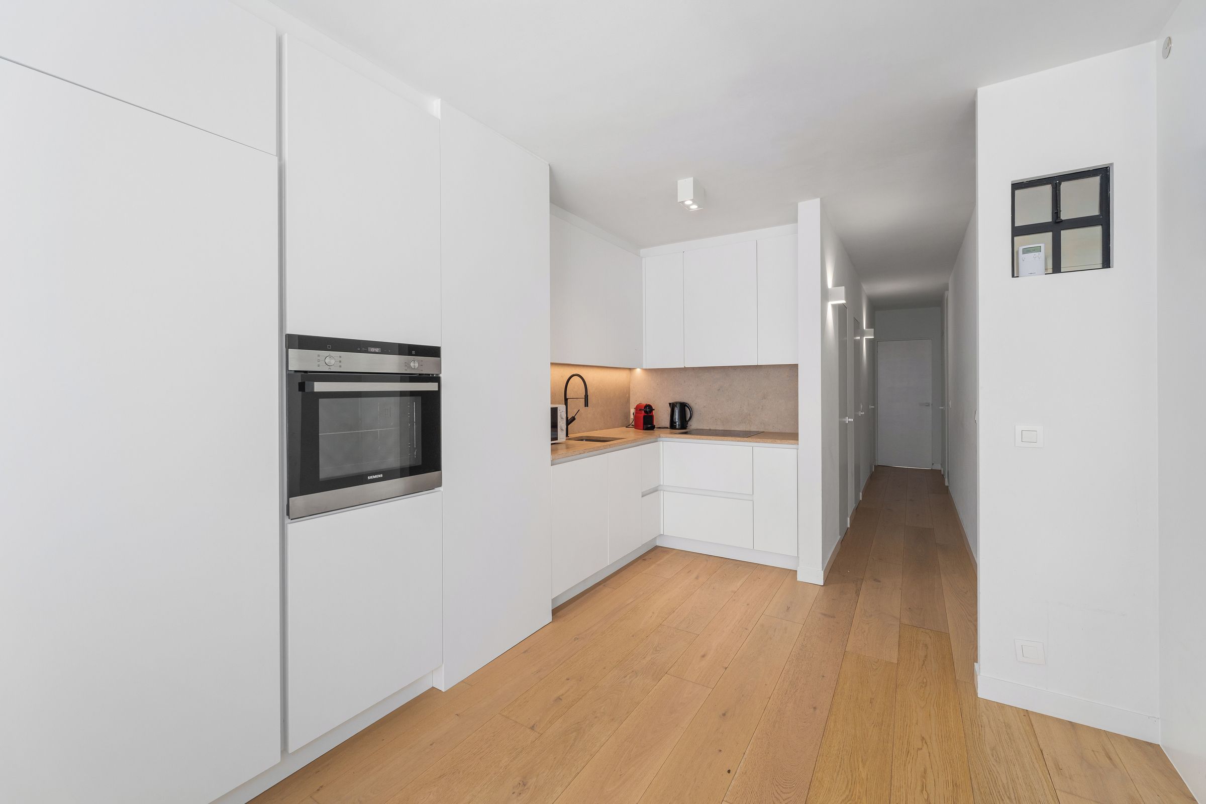 Une cuisine moderne avec des meubles blancs, un four encastré et un plancher en bois.