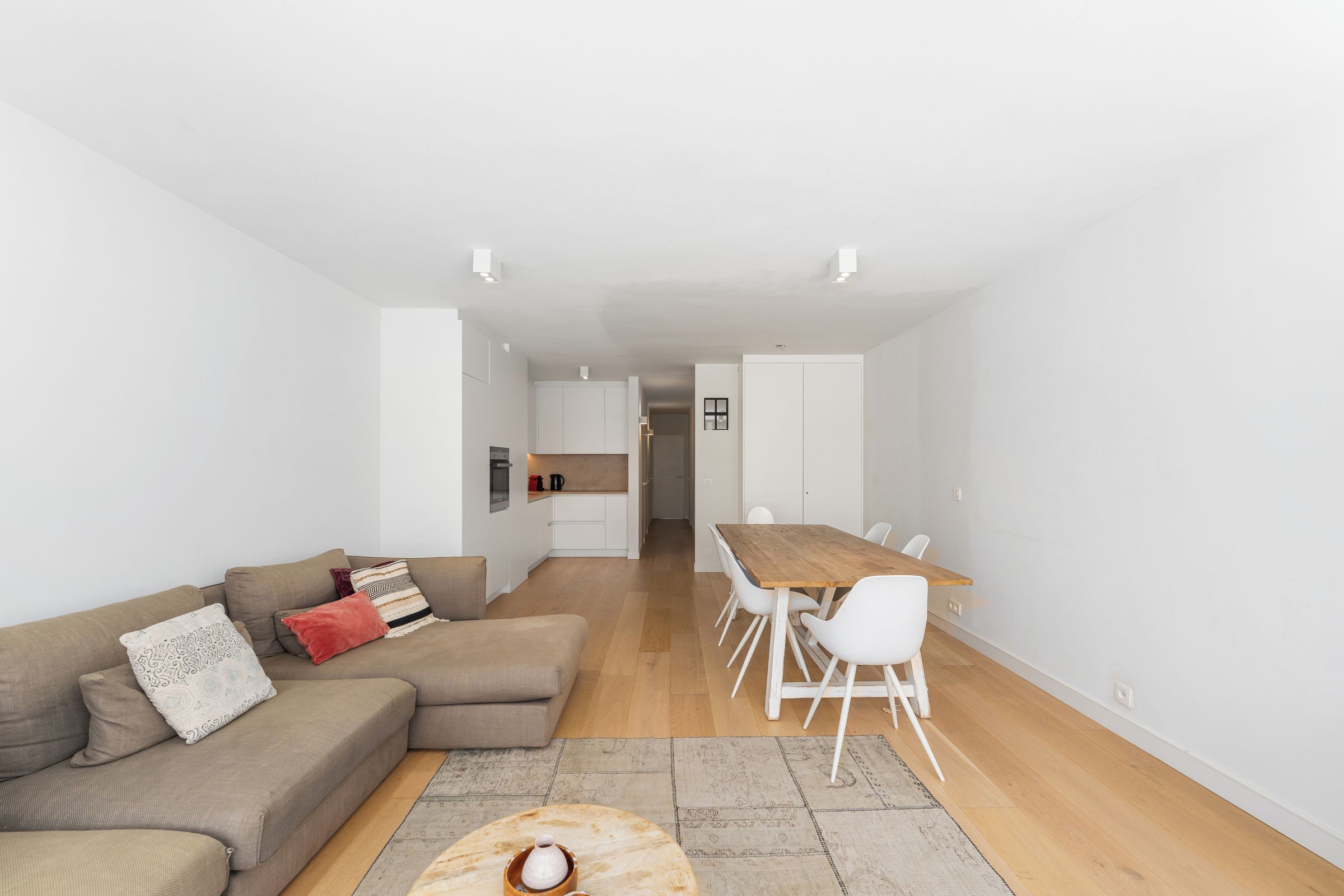 A modern living space with a sofa, a dining table with chairs, and a kitchen area.