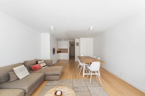 A modern living space with a sofa, a dining table with chairs, and a kitchen area.