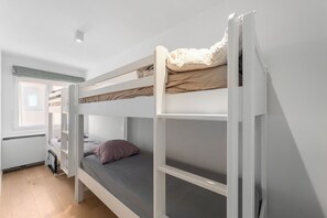 Une chambre avec un lit superposé, une fenêtre, un radiateur et une porte.