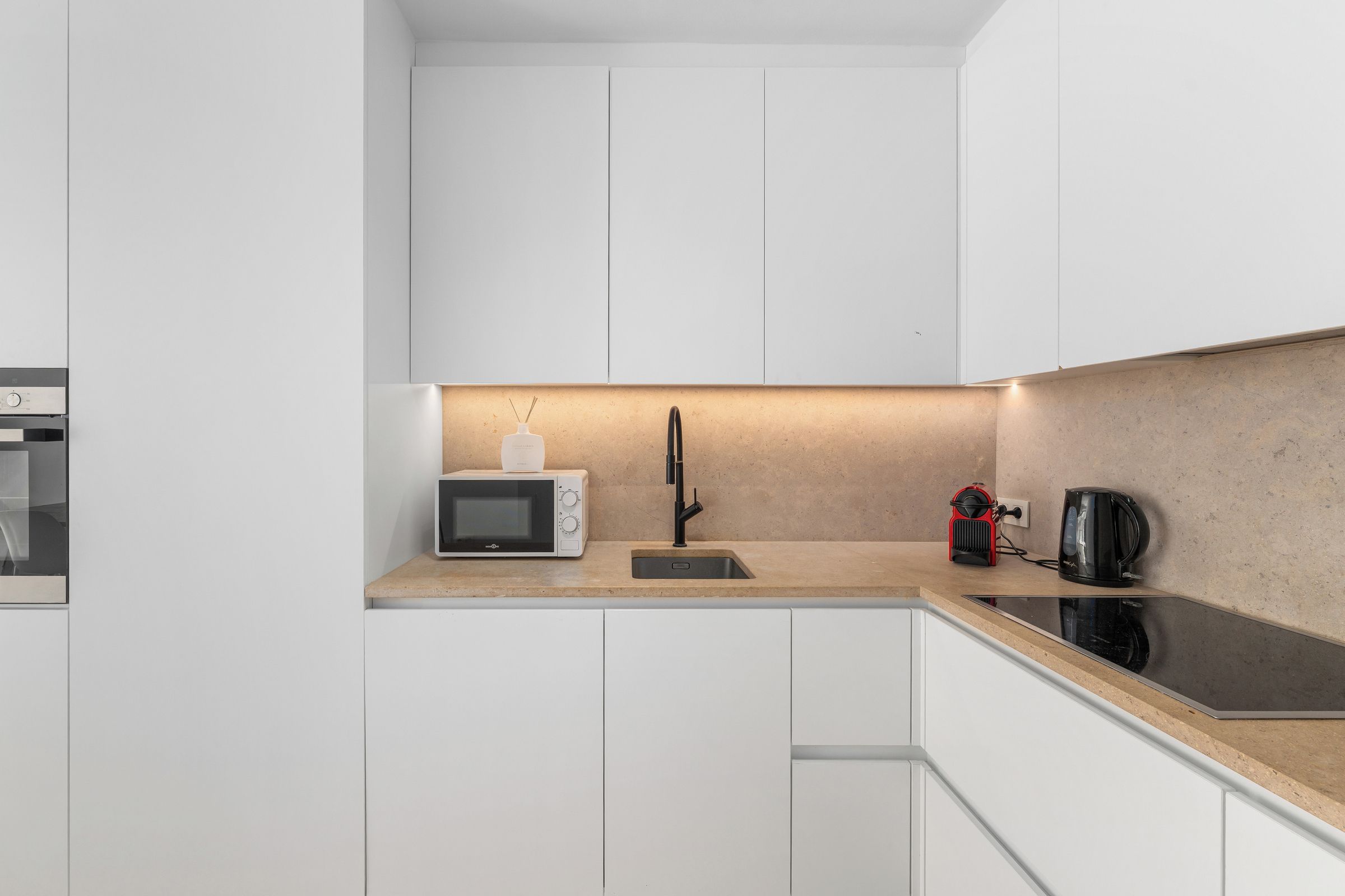 Una cocina moderna con armarios blancos, microondas, lavabo y cafetera.