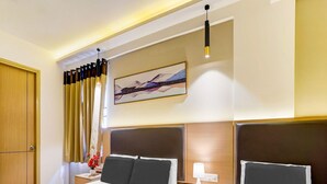 A hotel room with two beds, a nightstand with a lamp, a painting on the wall, and a window with curtains. - Deluxe With Twin Bed Hotel Metro Park (Bengaluru)