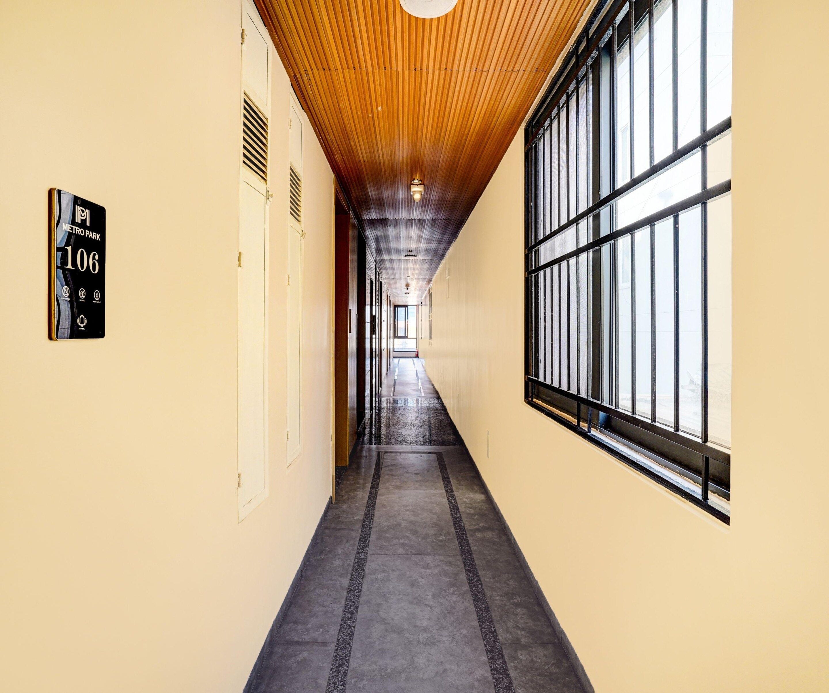 A corridor with a wooden ceiling, a sign indicating room number 106, and large windows on one side.
