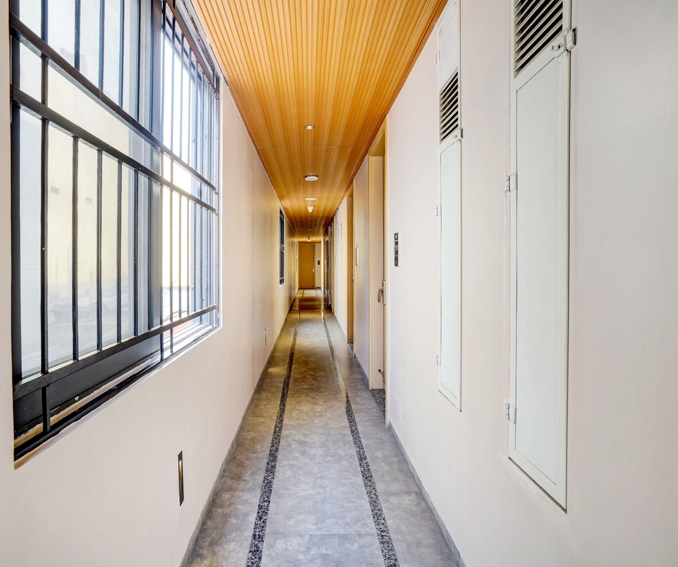 Un pasillo con techo de madera, ventanas amplias a un lado y suelo de hormigón.