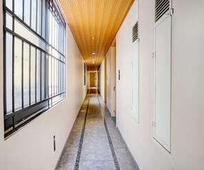 A hallway with a wooden ceiling, large windows on one side, and a concrete floor. - Deluxe With Twin Bed Hotel Metro Park (Bengaluru)