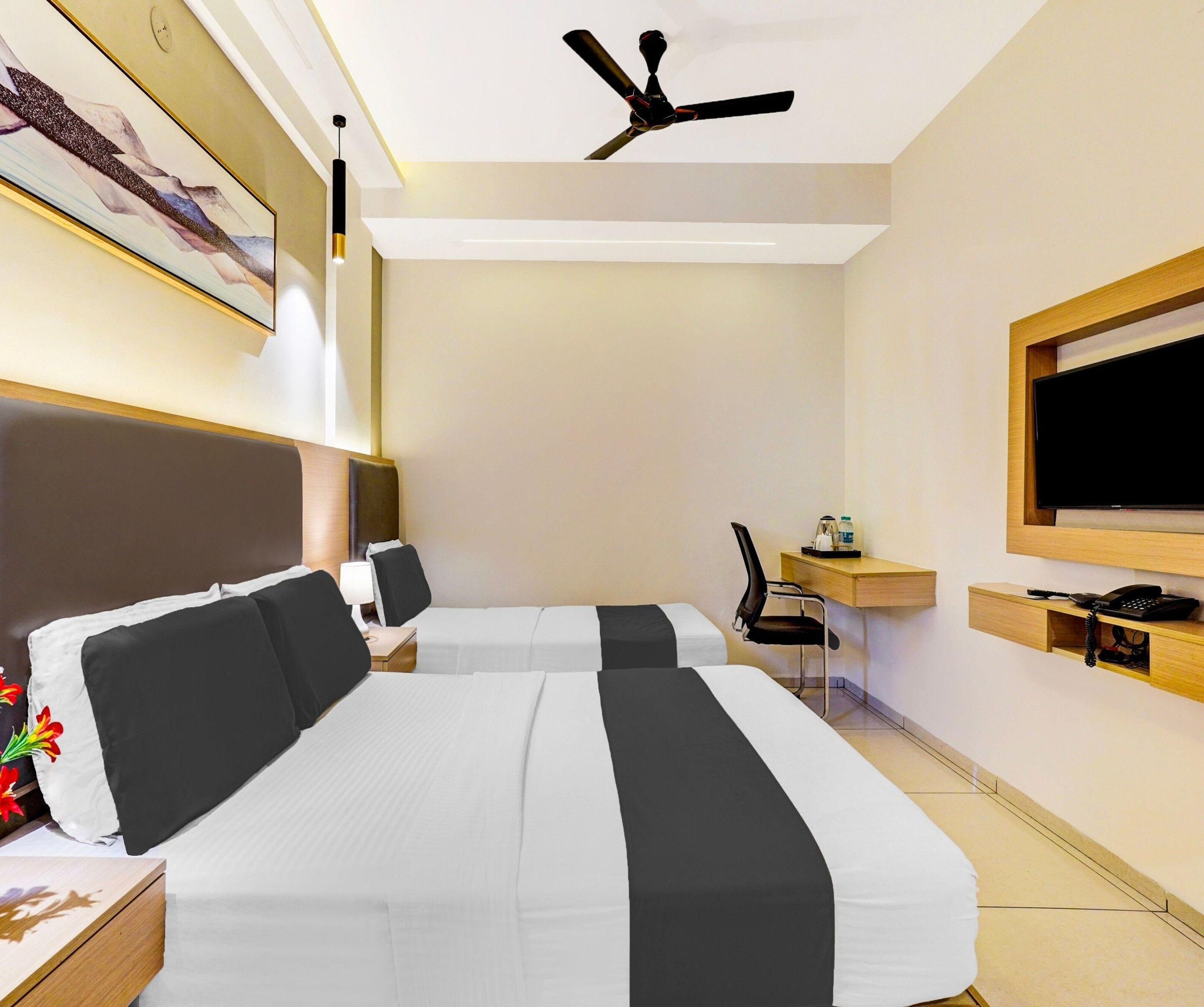 Hotellihuone, jossa on kaksi sänkyä, työpöytä, tuoli, televisio ja kattotuuletin.