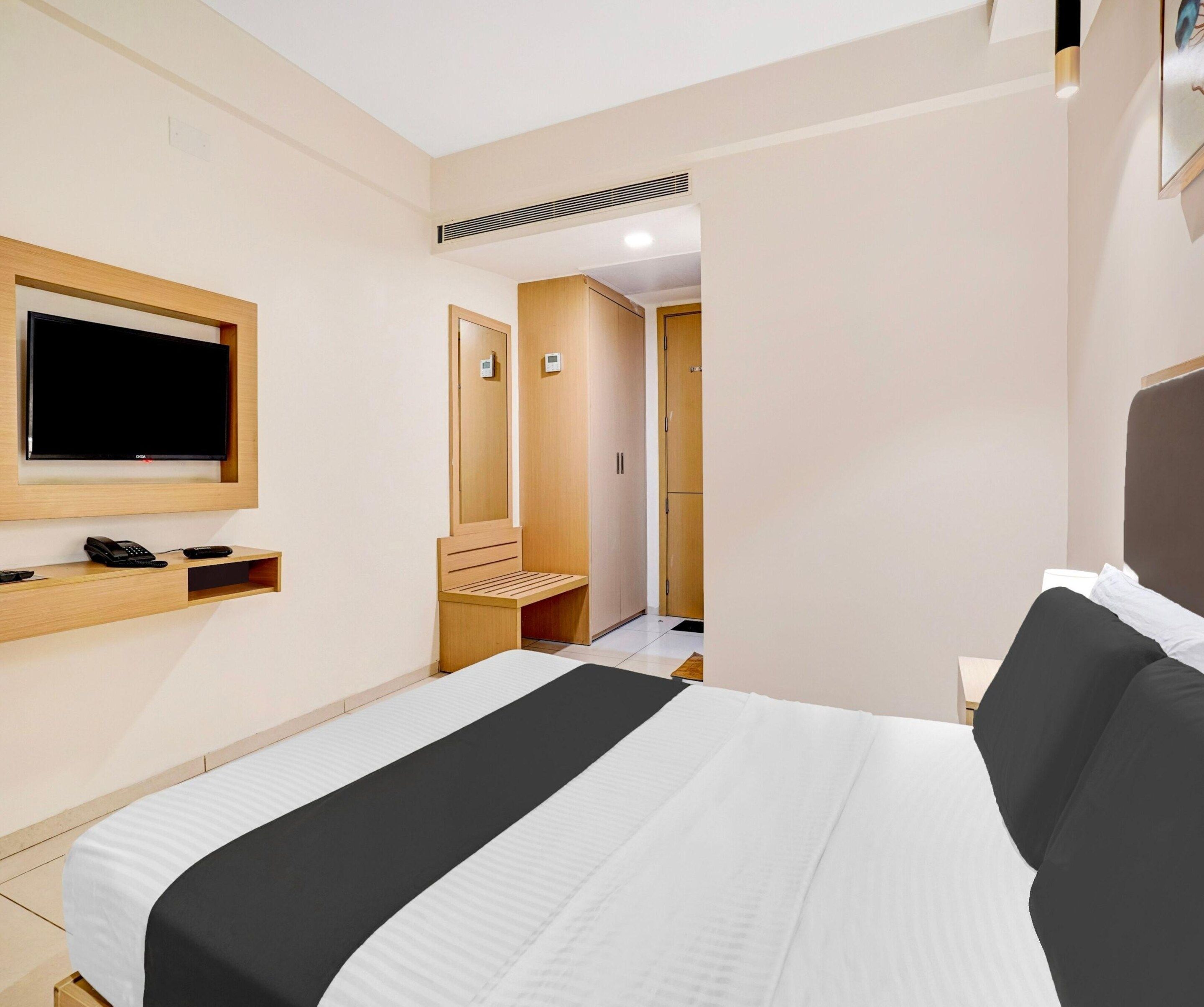 A hotel room with a bed, a TV mounted on the wall, a desk with a phone, and a wardrobe.