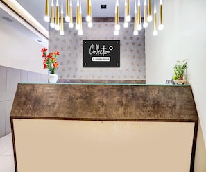 A reception desk with a sign that reads 'Collection Company-Serviced.' There are two potted plants on the desk. - Deluxe With Twin Bed Hotel Metro Park (Bengaluru)