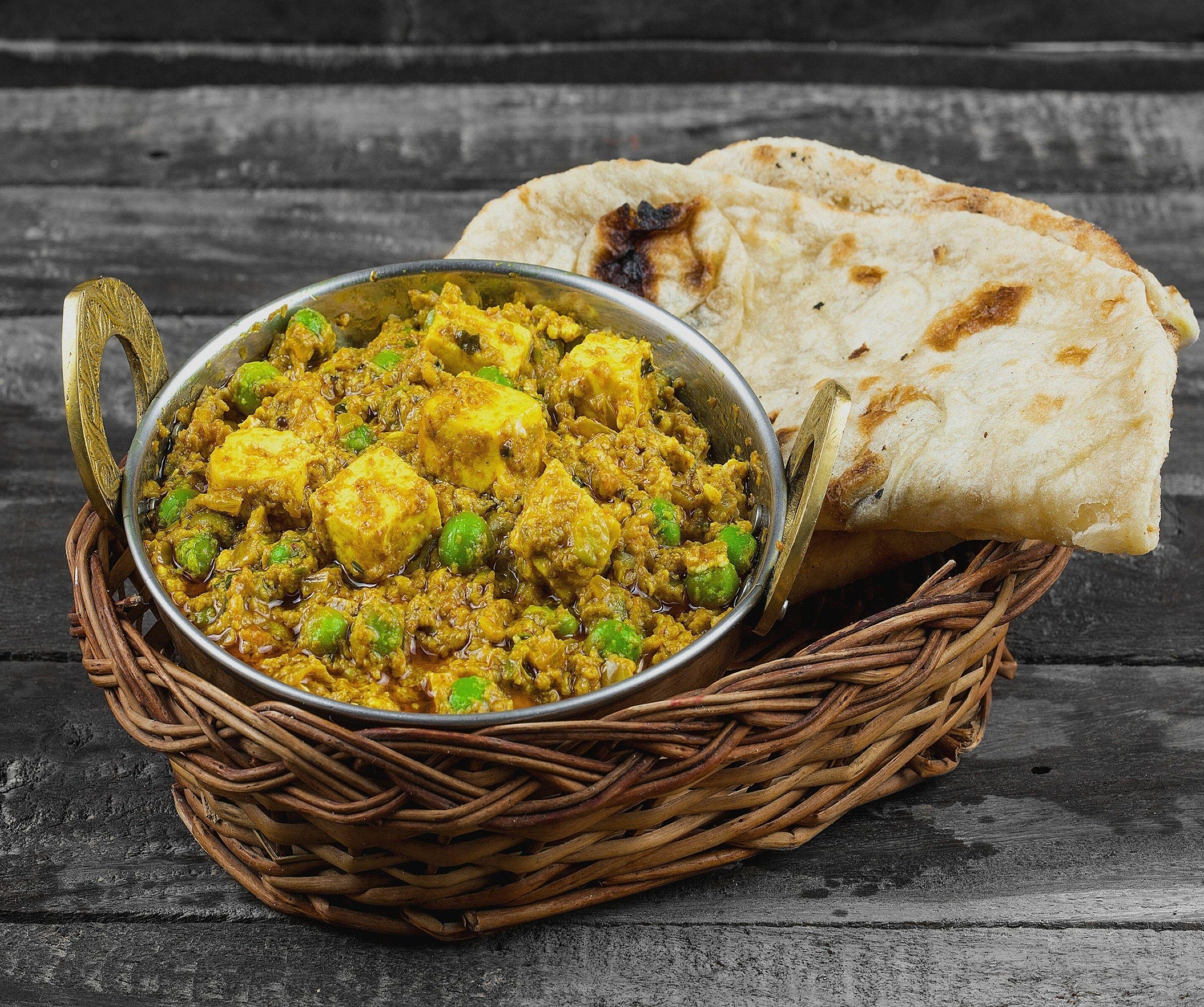 A meal of paneer curry with naan bread on a rustic wooden table.