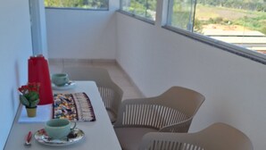 Quarto com mesa e cadeiras, janela com vista para vegetação e colinas, e luminária pendente.