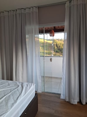 A bedroom with a bed, a sliding glass door leading to a balcony, and a view of a hilly landscape.