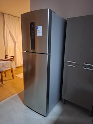 A stainless steel refrigerator with a digital display and a small sticker, next to a dark-colored cabinet with two drawers. - New apartment in Santa Teresa-ES, enclosed balcony with mountain views. (Santa Teresa)