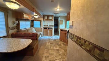 A compact RV interior with a kitchenette, a dining area, and a seating space.