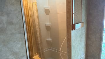 A corner shower with a tiled wall and a wooden door frame.