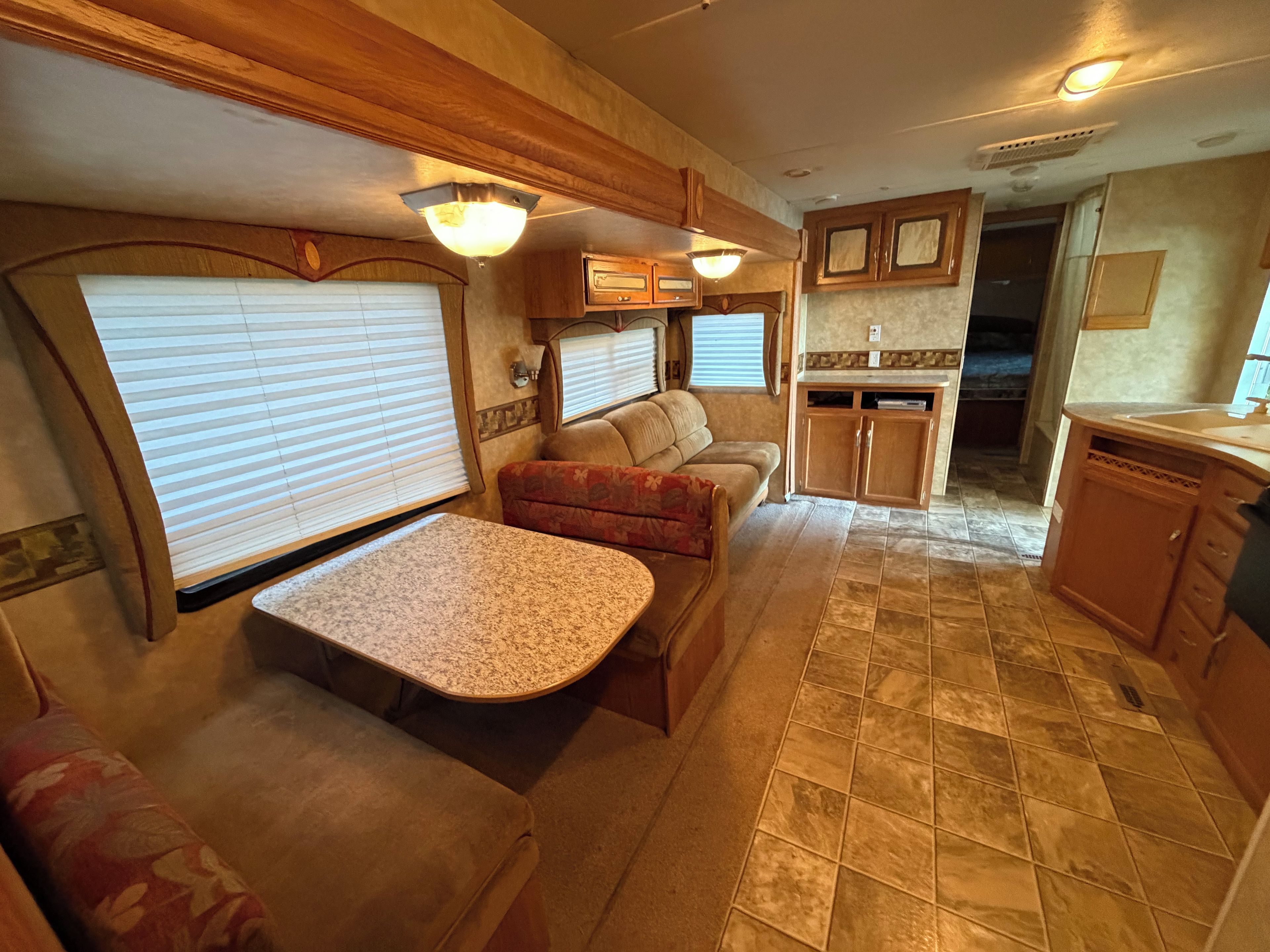 Interior compacto de una caravana con kitchenette, zona de estar y mesa de comedor.