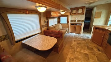 Interior compacto de una caravana con kitchenette, zona de estar y mesa de comedor.