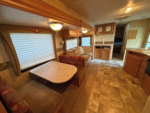 A compact RV interior with a kitchenette, seating area, and a dining table.