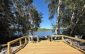 A wooden deck leading to a lake with a clear view of the water and surrounding trees. - Hidden Lakeside Retreat! Camper + Bunkhouse in Charming Sawyer. (Sawyer)