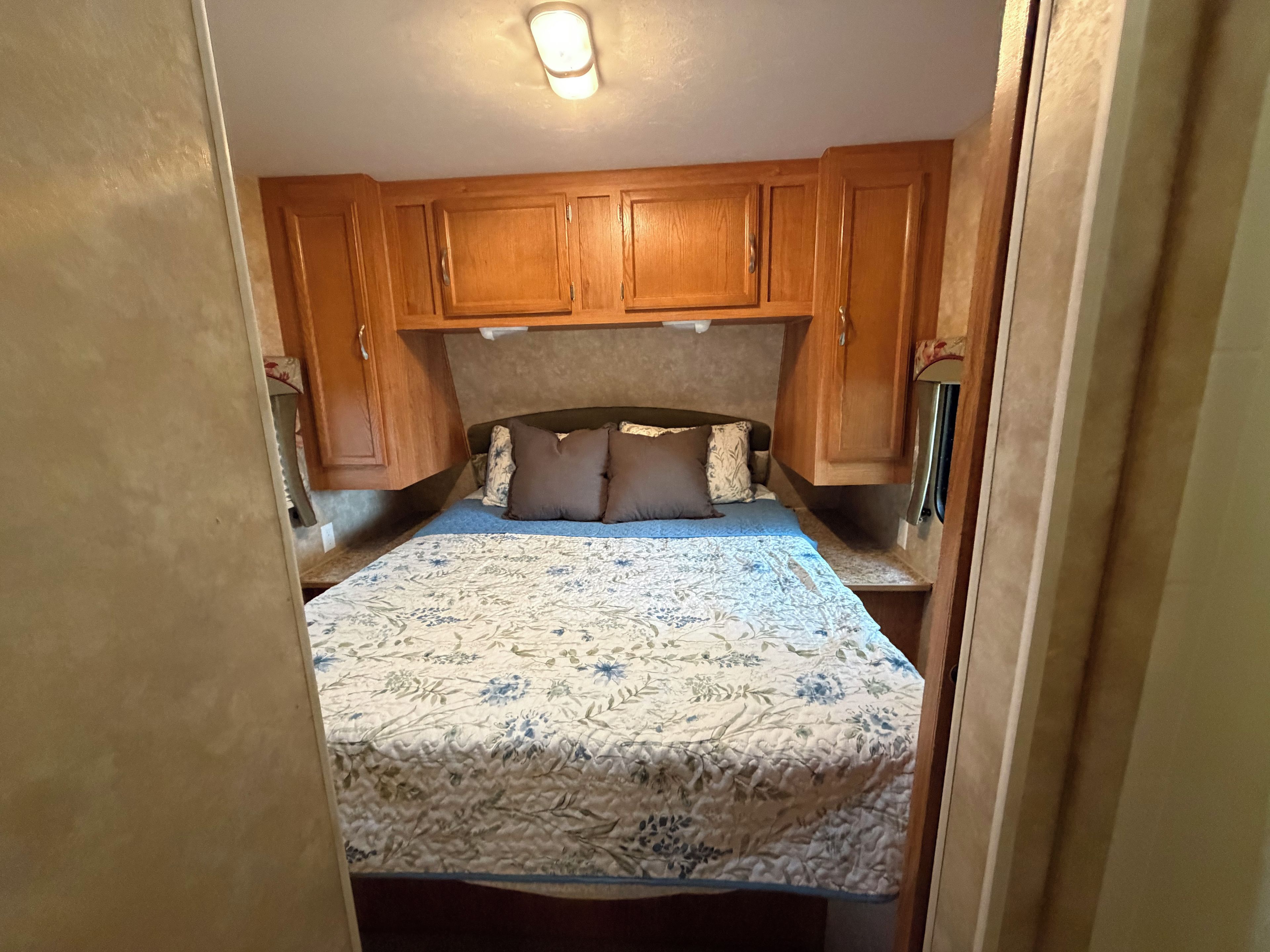 A compact bedroom with a bed, wooden cabinets, and a ceiling light.
